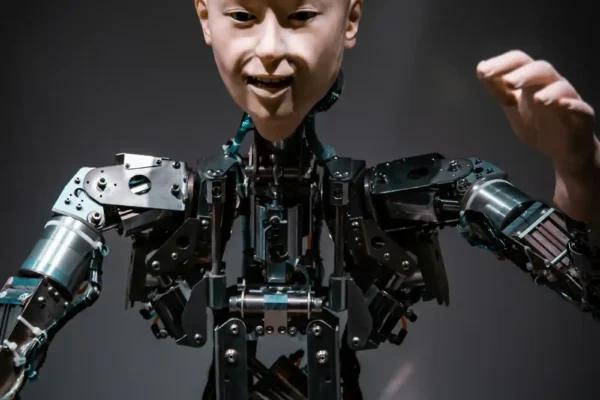 Robot con apariencia humana con razonamiento artificial, con el brazo izquierdo levantado a la altura de la cabeza, sobre fondo gris.
